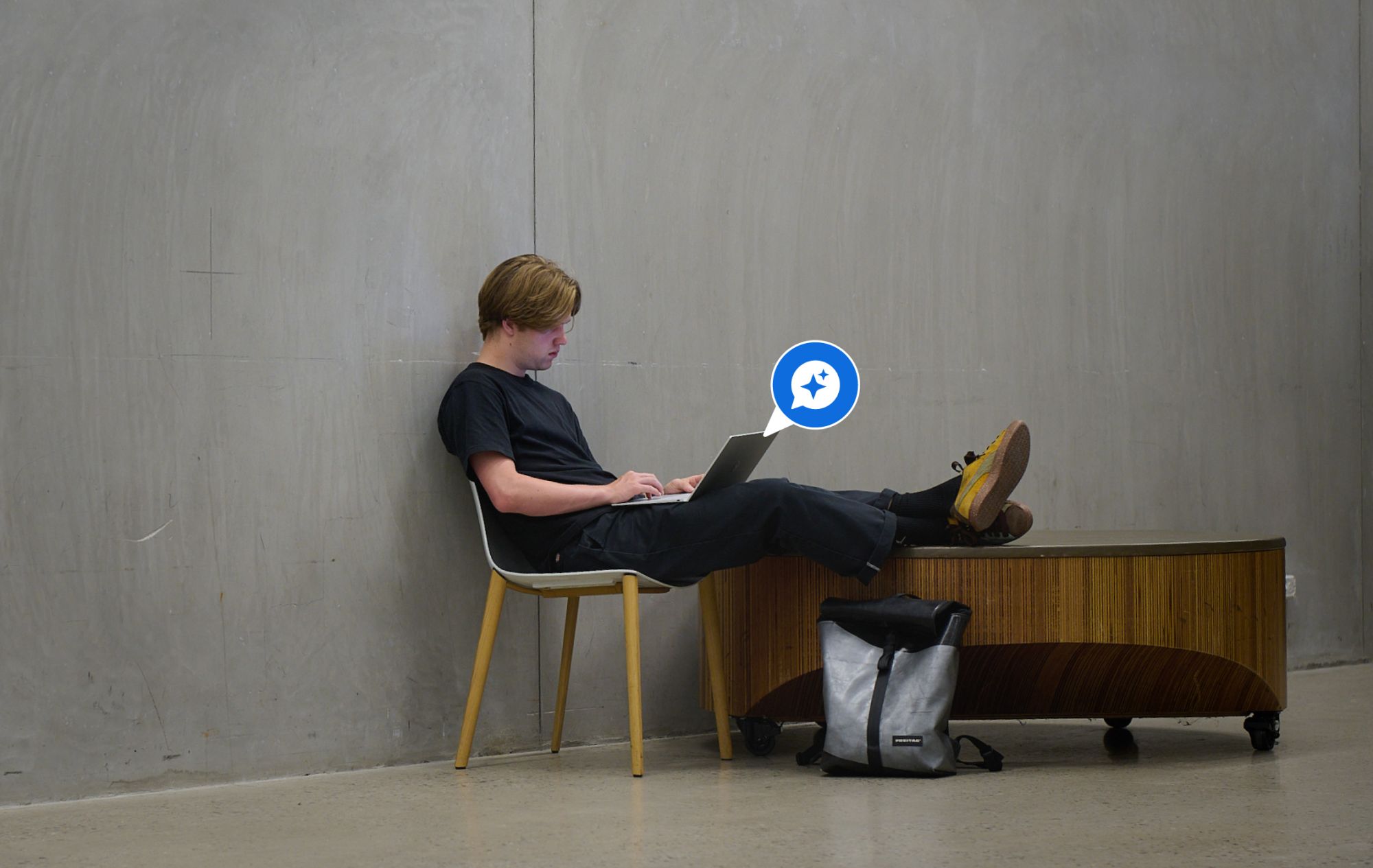 A student sits reclined with a laptop displaying a glowing chat icon.