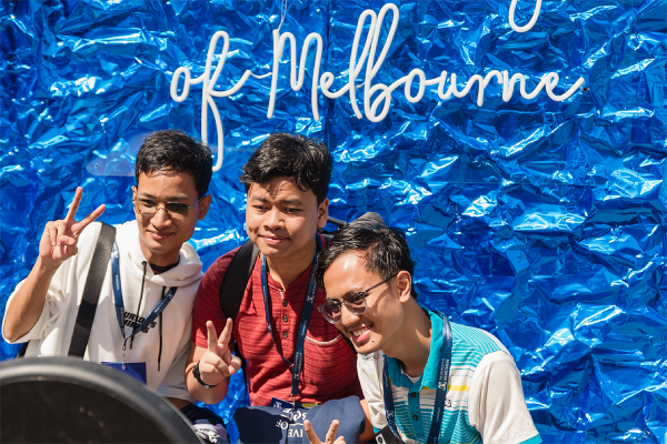 Three students making peace sign gestures for photo with blue backdrop
