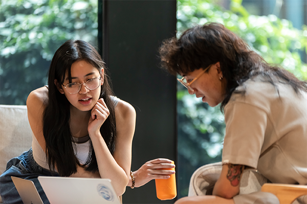 two students sitting together at a table looking at a laptop