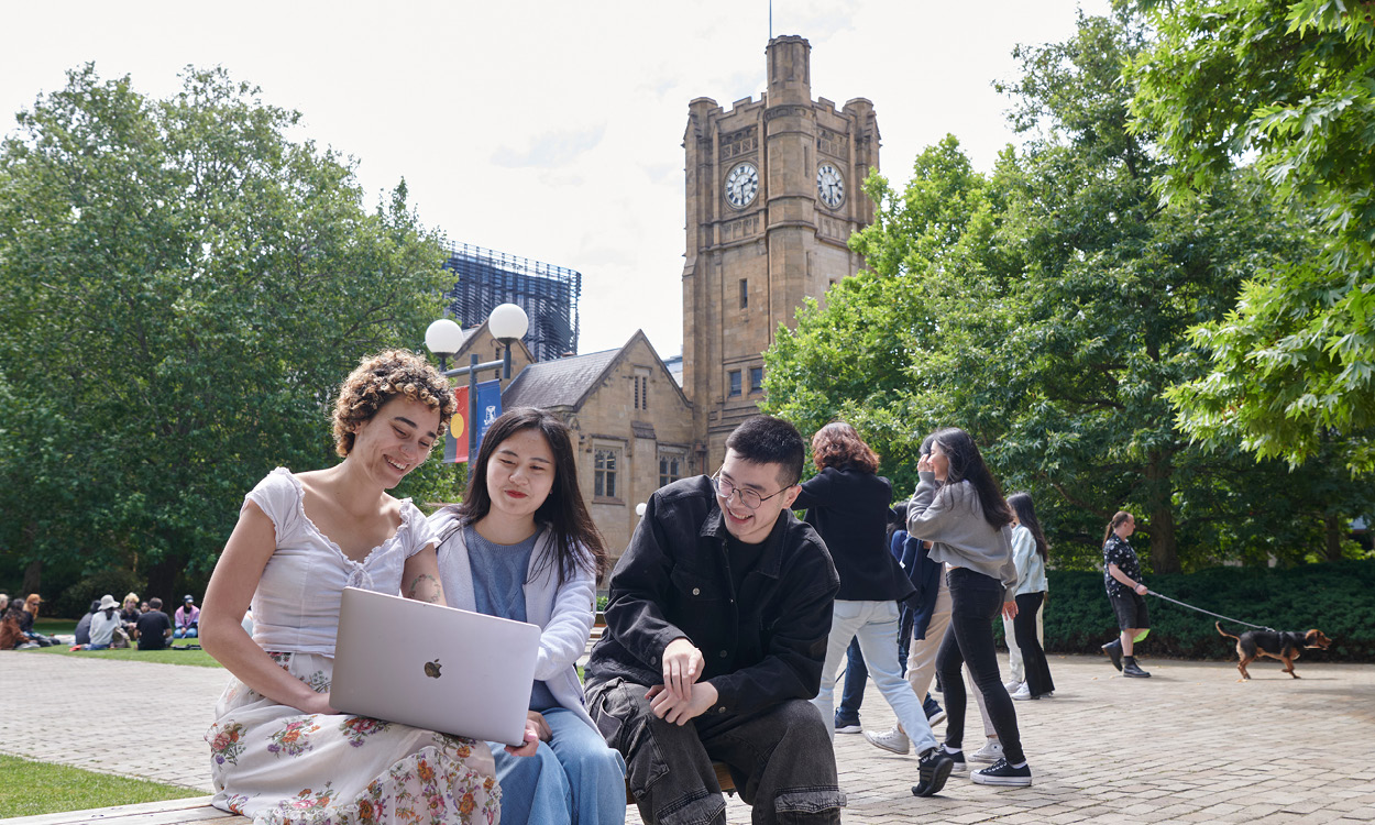 Option 1 (recommended): Students using a laptop in a campus courtyard with the university clock tower in the background.
