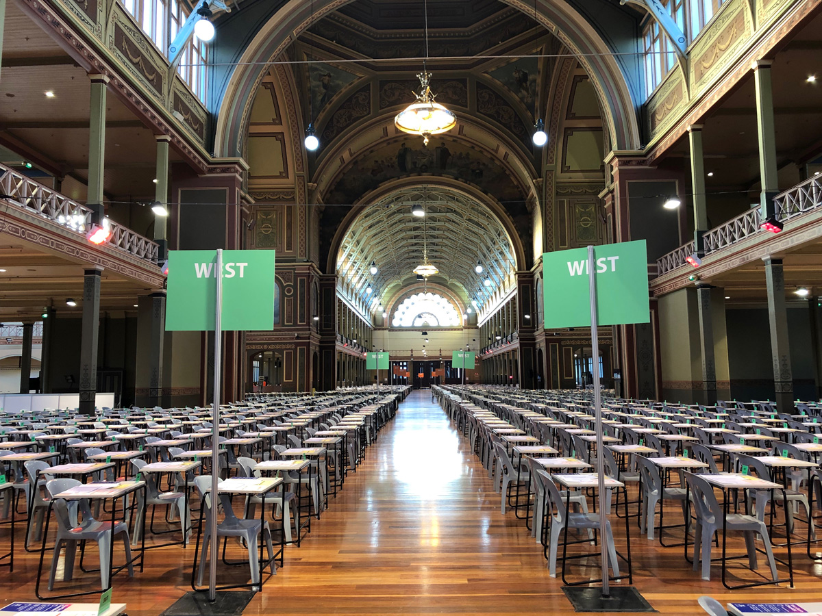 Many rows of individual chairs and tables for exams, with signs reading "West"