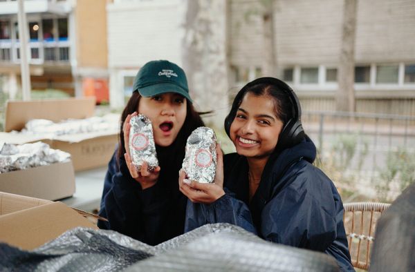 Two students smiling and holding up burritos 