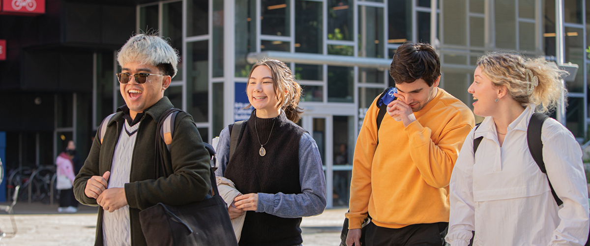 Four students walking and smiling on campus.