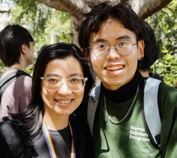 Two people smiling at the camera, one with a rainbow lanyard and one with a 