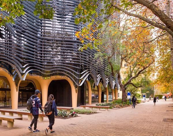 Two students walk past the distinctive wavy facade of the Melbourne School of Design building during autumn.