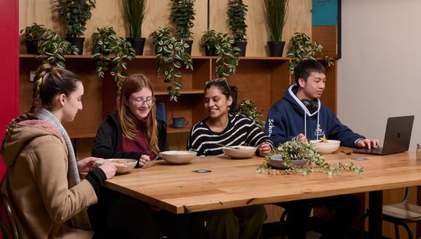 Four students sitting at a wooden table inside the Parkville Campus Canteen.
