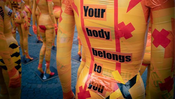 Art installation featuring a large group of mannequins covered in masking tape and various wording.