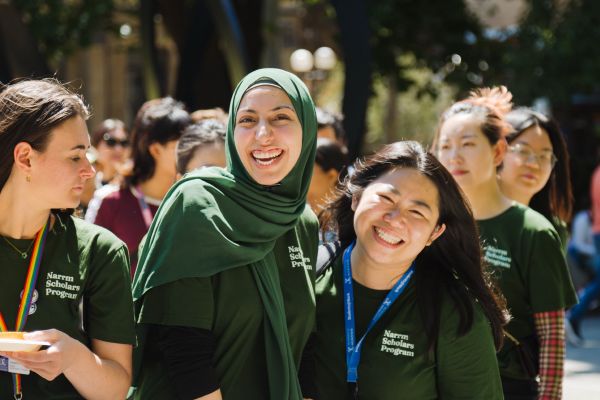 Two young women in green Naarm Scholars Program shirts smiling brightly at the camera