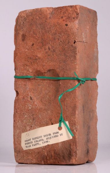 Heart Imprint Brick 2018. The image is a ochre brick wrapped in green ribbon, with a heart imprinted on it's "chest"