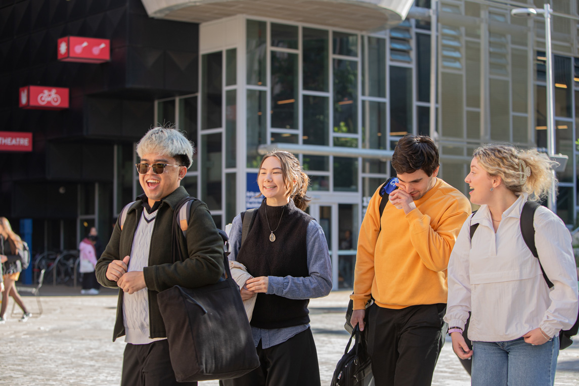 Four young people walk and laugh outdoors.