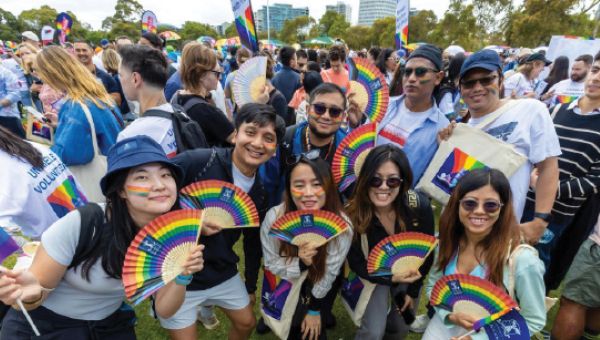 Group of smiling students holding paper fans that display the rainbow pride flag colours.