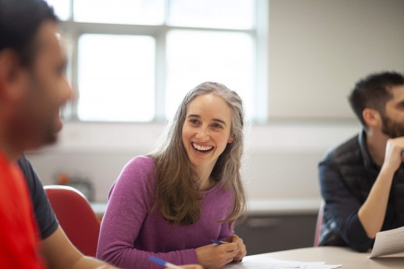 Woman in focus smiling with a group of students in a classroom
