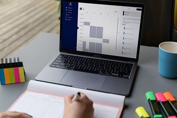 Image of laptop with class timetable showing and persons hands taking notes with highlighters in front of laptop.