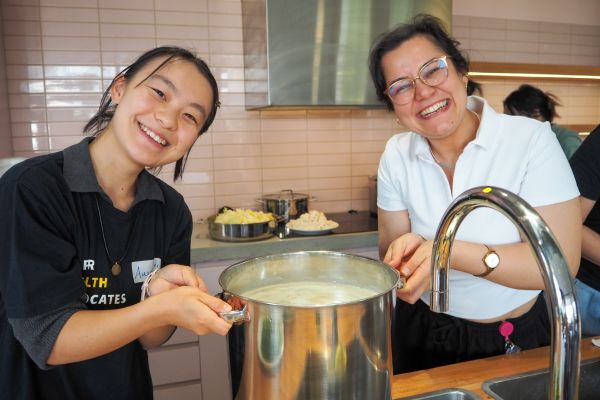Two people at a Cooking Workshop holding a huge pot and smiling