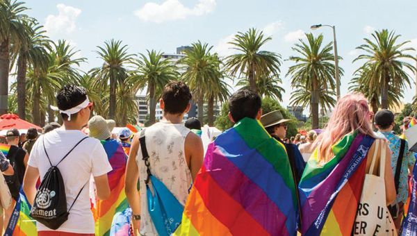 Four students with their backs to camera walking through the marshalling area of the Midsumma Pride March.