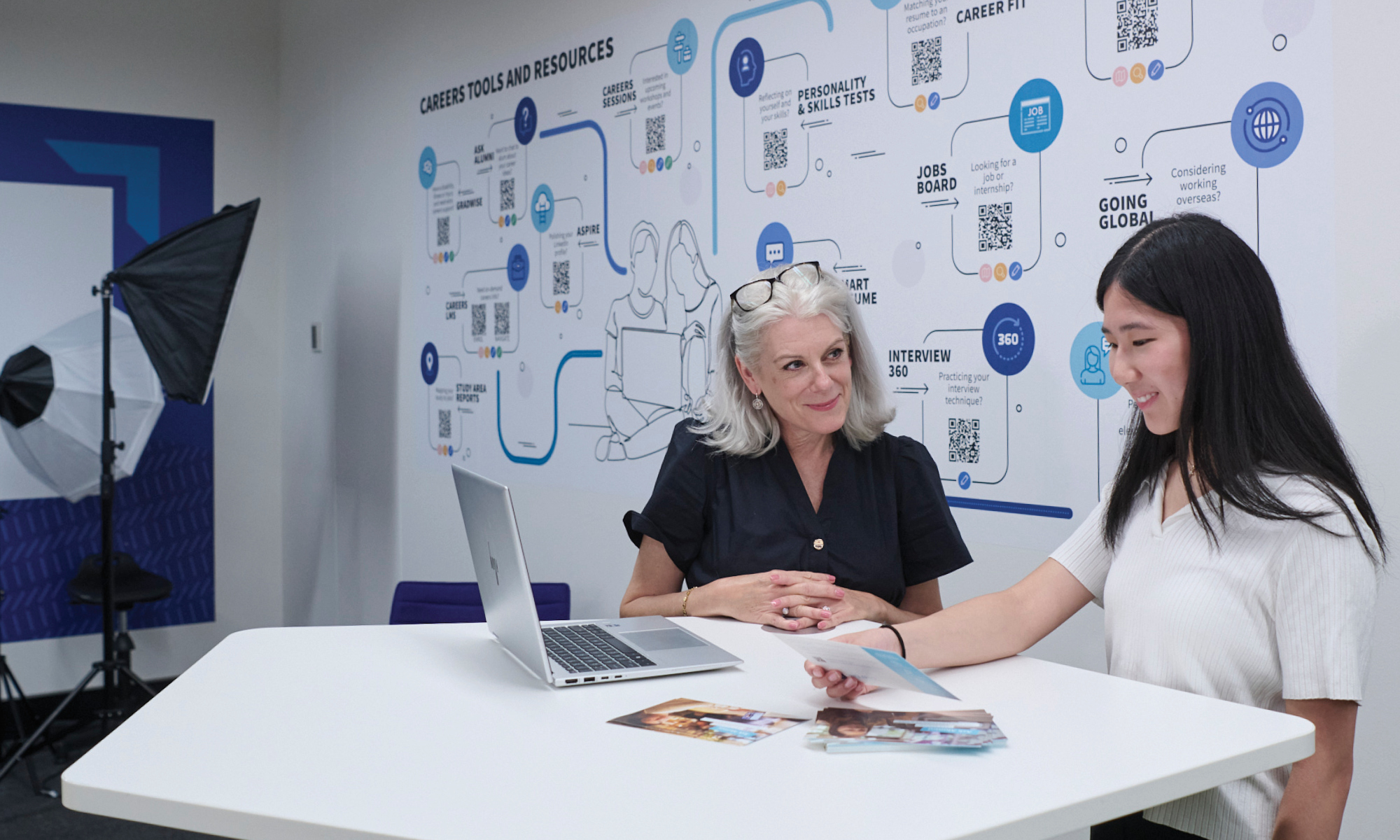 Two women at a table looking at laptop and career-related resources