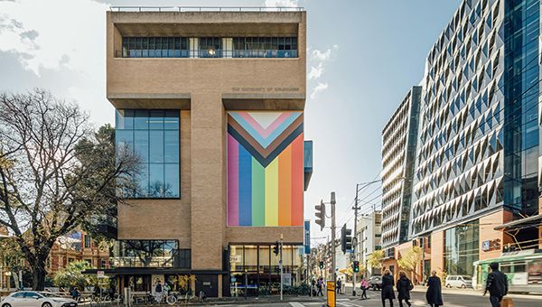Exterior image of campus Building 199 with a large vinyl progress pride flag hung on the side of the building.