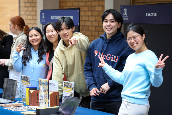 Five students at information stall, one pointing to camera