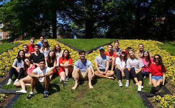 Group of overseas students relaxing together on a grassy campus area during an outdoor study experience.