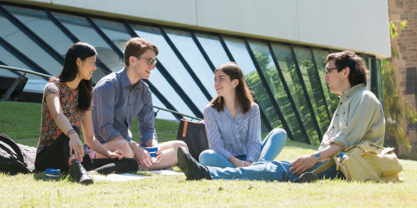 Four students sitting on grass and talking outside the Melbourne School of Design.