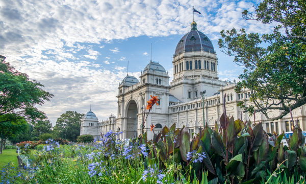 Historic exhibition building with a domed roof surrounded by gardens and flowering plants.